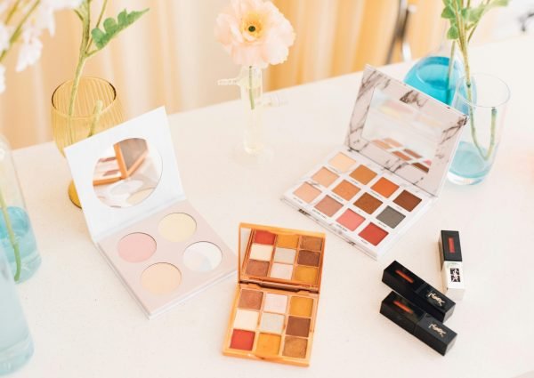 Aesthetic display of makeup palettes and lipsticks surrounded by flowers.